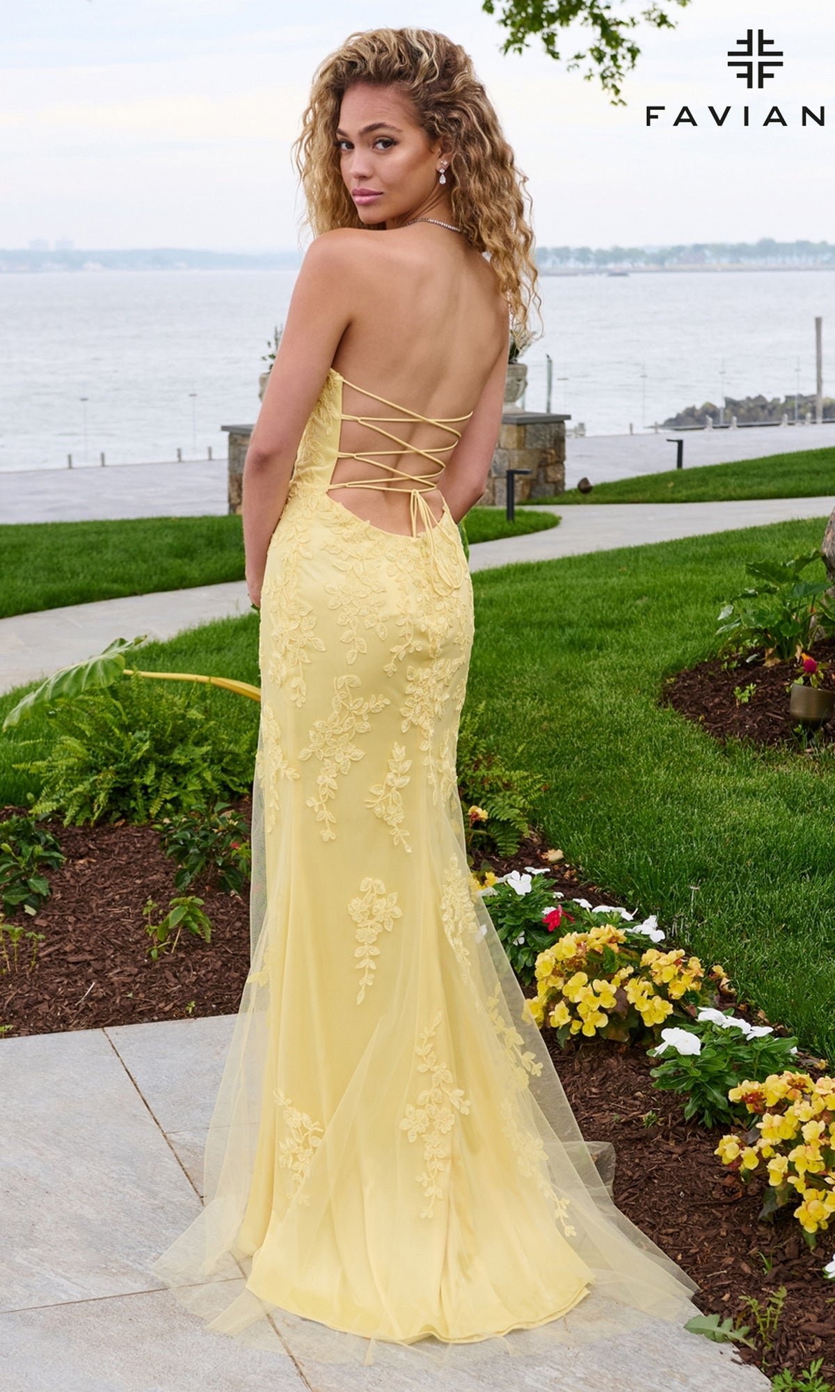 A back view of a person wearing a Long Prom Dress: Faviana 11627, a pale yellow strapless column dress with intricate lace appliques and a lace-up corset back.